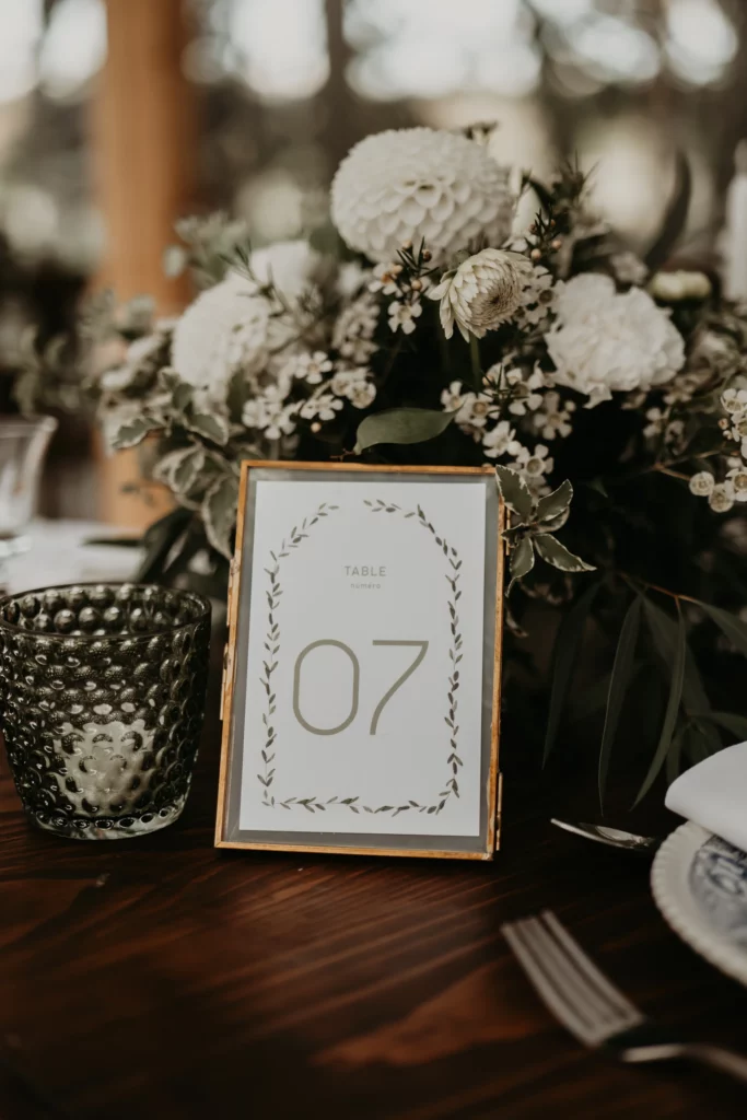 Numéro de table posé sur une table de mariage élégamment décorée, avec composition florale blanche et bougie, à La Maison Villeneuve. Exemple de détail soigné illustrant les bonnes pratiques évoquées dans l’article sur les erreurs à éviter en décoration de mariage.