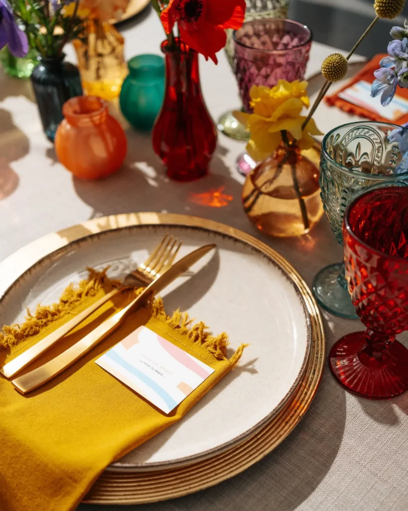 Table colorée avec verrerie brillante, fleurs vives et serviette ocre créant une ambiance dîner mariage joyeuse et lumineuse.