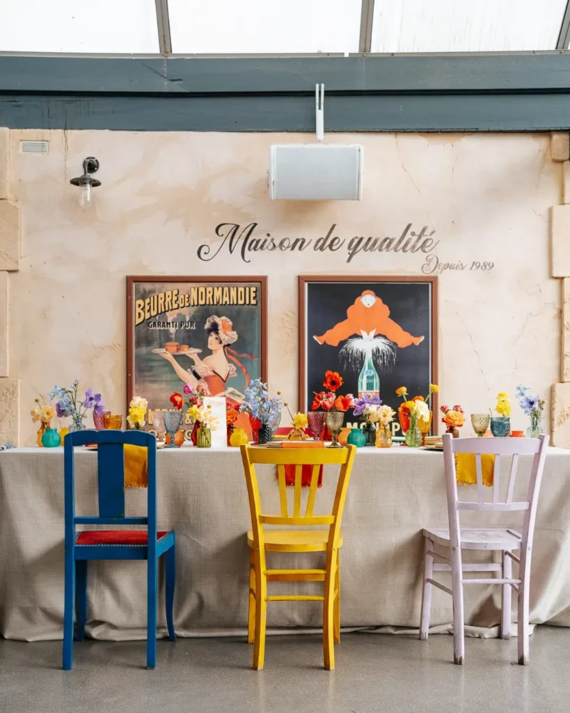 Table de mariage colorée associant chaises dépareillées, compositions florales vives et ambiance lumineuse naturelle pour une décoration équilibrée. Mobilier