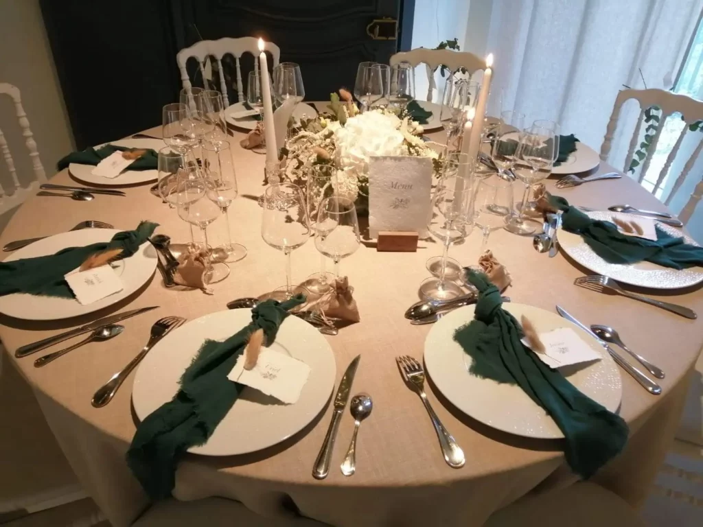 Table de mariage naturel chic avec nappage beige, centres floraux blancs et touches de vert profond.
