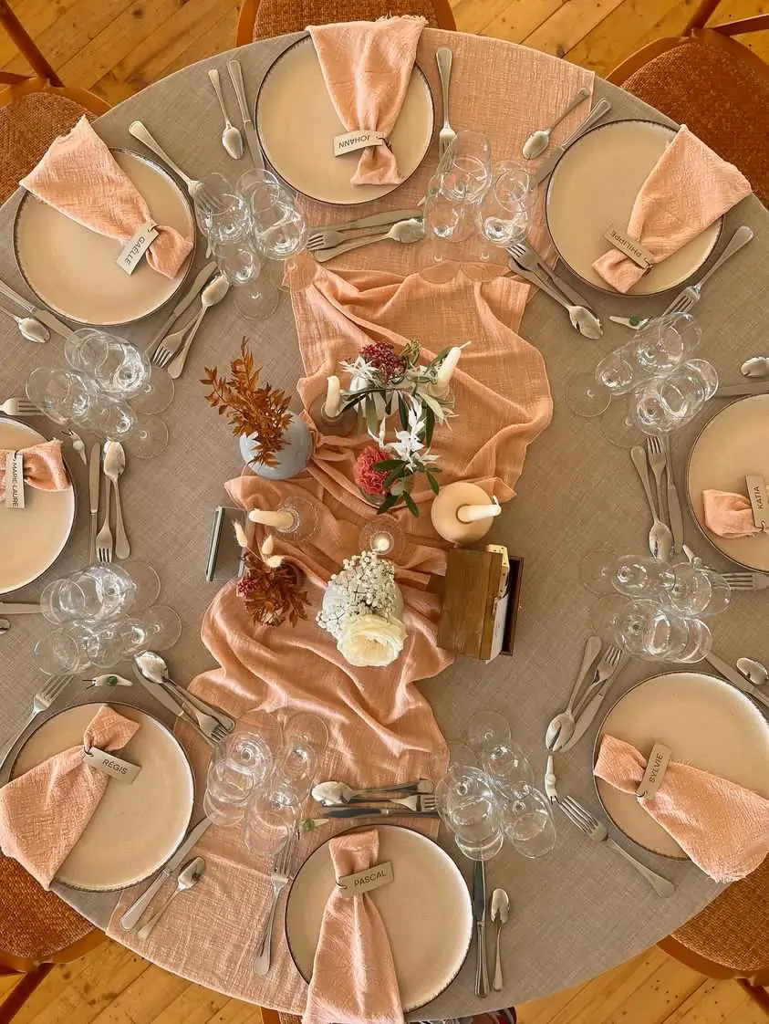 Chemin de table pêche pour sublimer une table de mariage élégante. Chemin de table en tissu pêche drapé sur une table ronde de mariage avec une décoration douce et naturelle.