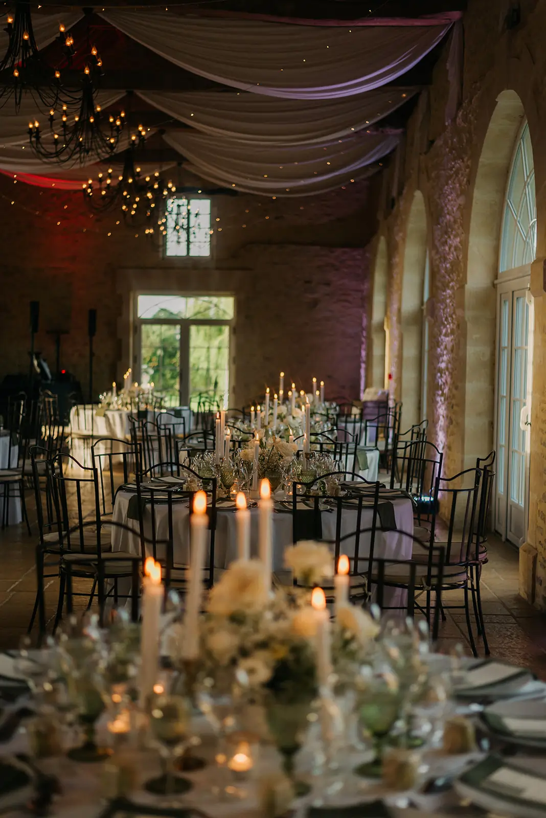 Table de mariage élégante mise en scène avec un art de la table raffiné, chandeliers et compositions florales blanches dans une salle en pierre.
