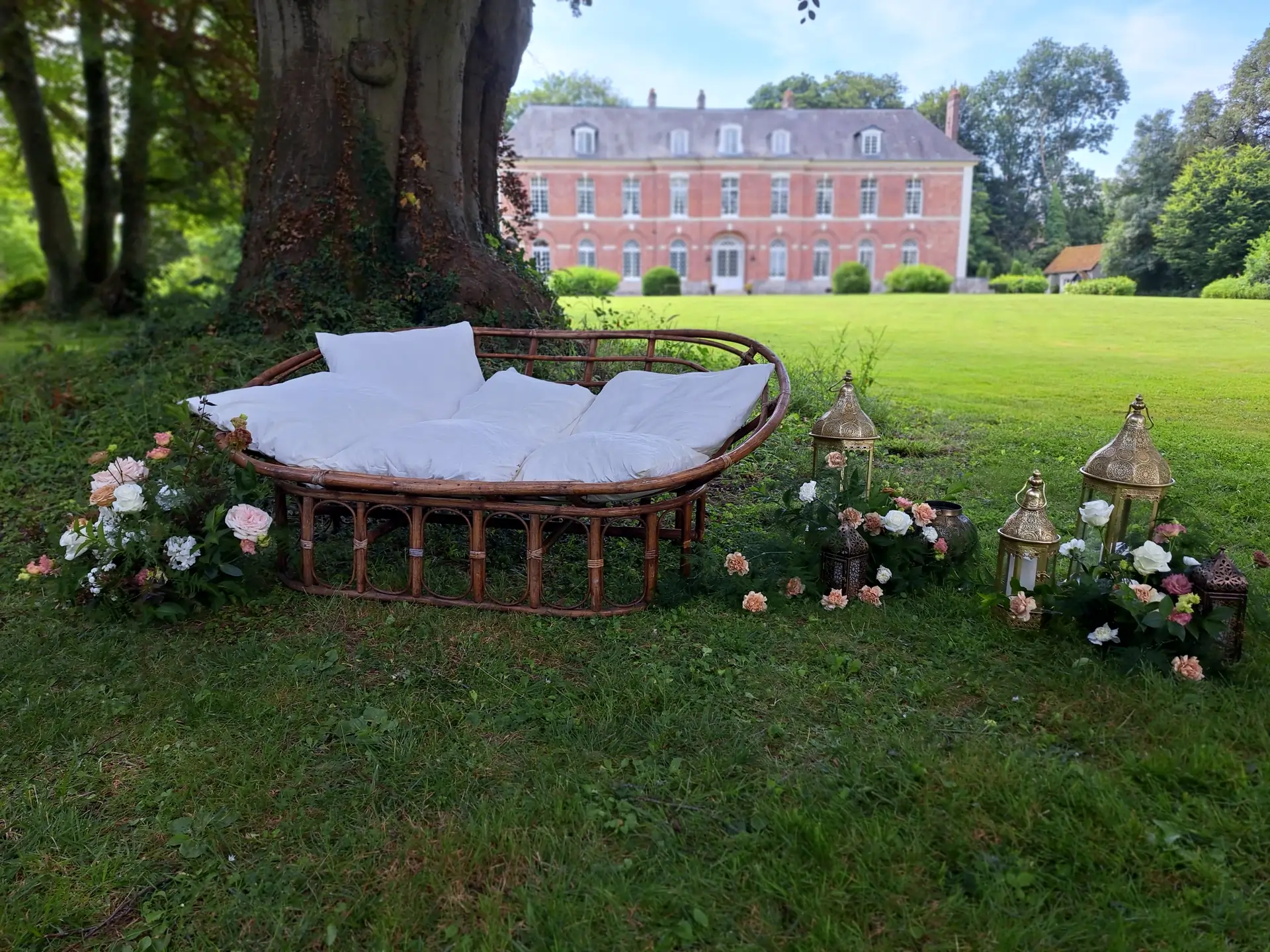 Loveuse Blaise installée en extérieur au pied d’un arbre, décorée de fleurs et lanternes dorées dans un parc de château.