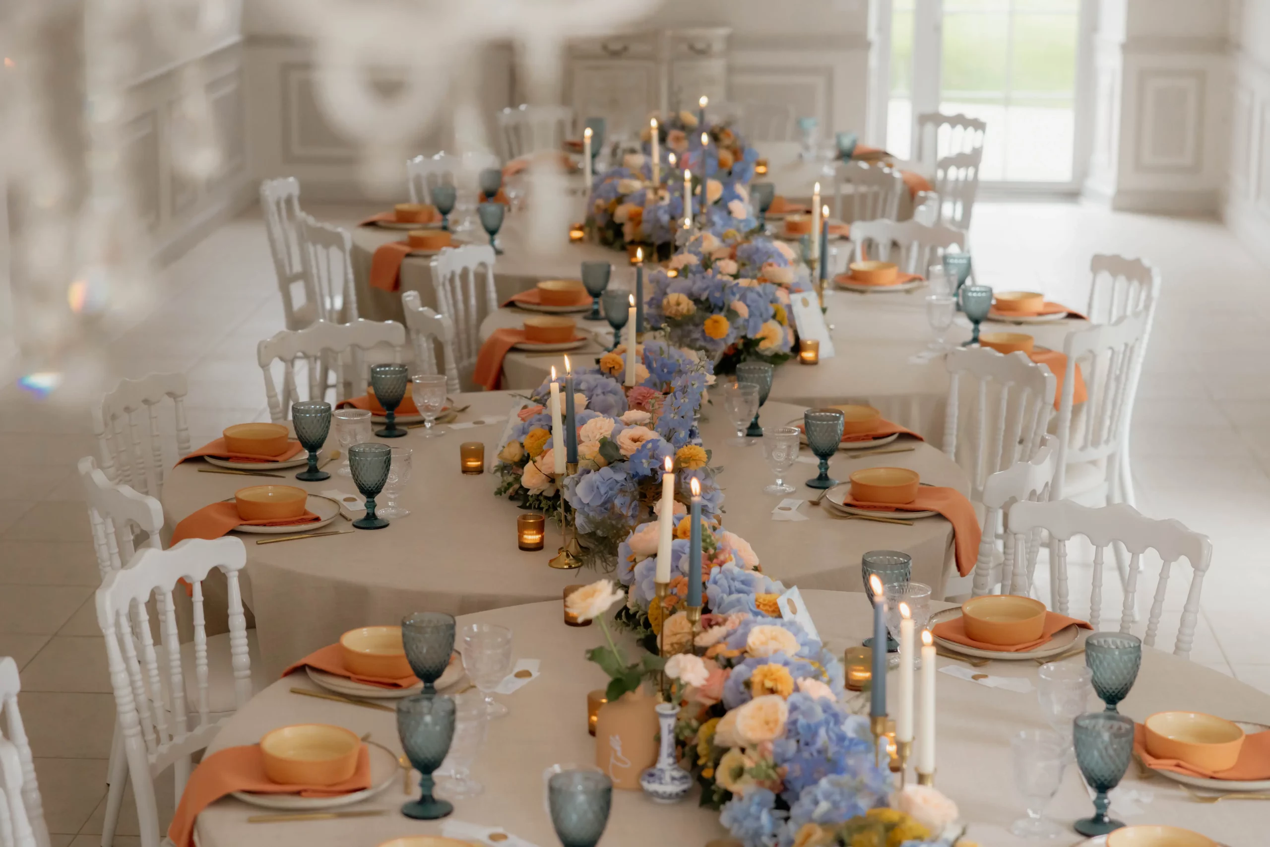 Tables rondes collées et décor pastel pour une tablée harmonieuse Tables rondes collées formant une longue tablée, décorées de fleurs pastel et de bougies pour un dîner de mariage élégant.