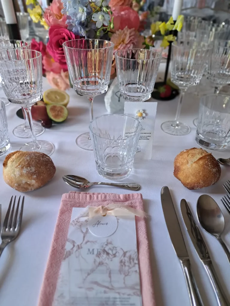 Art de la table mariage coloré avec verres ciselés, menu personnalisé et centre de table fleuri dans des tons vifs.