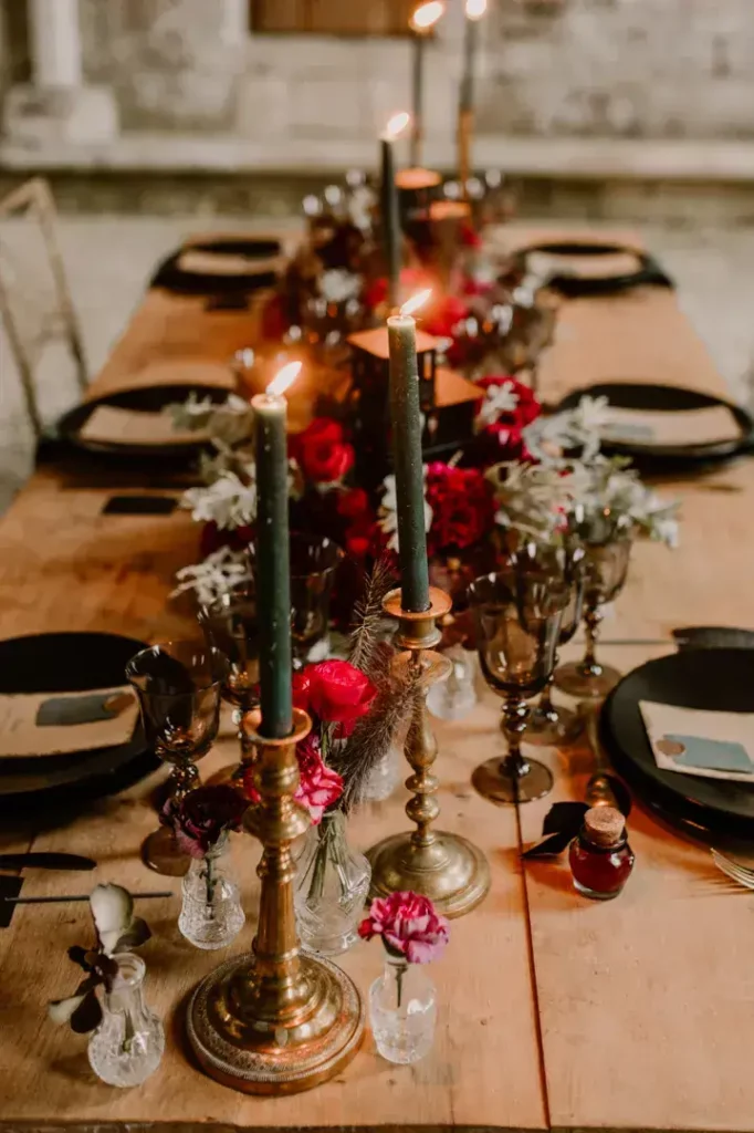 Art de la table mariage aux tonalités sombres avec chandeliers dorés, fleurs rouges et vaisselle noire pour un dîner élégant.