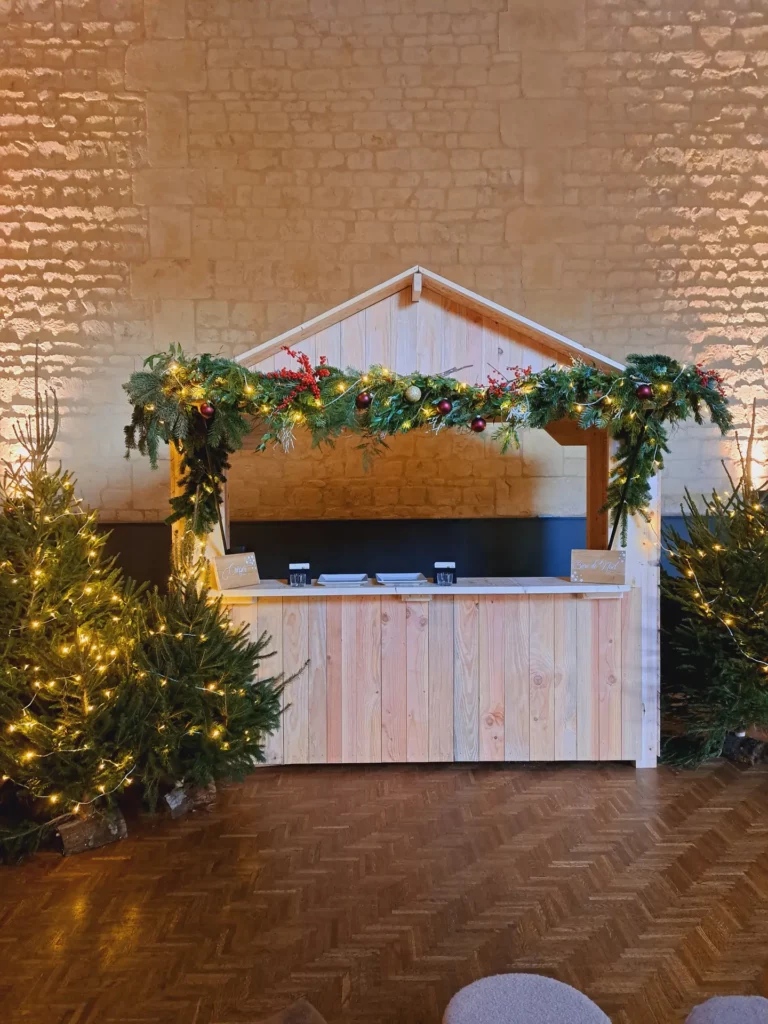 Chalet Johann en bois décoré de guirlandes de sapin et lumières, installé en intérieur avec des sapins illuminés.