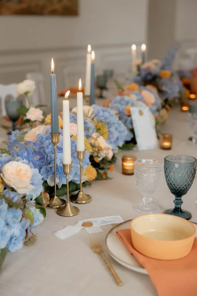 Bougies et composition florale posées sur une table issue d’un ensemble de tables rondes collées pour un dîner de mariage.