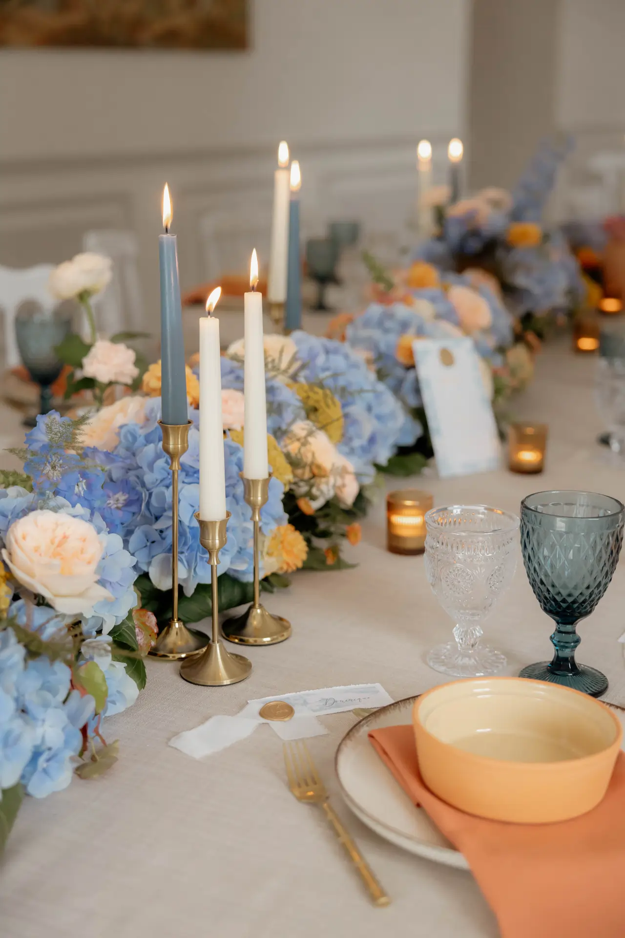 Location de bougeoirs et photophores pour mariage en Normandie. Bougies et composition florale posées sur une table issue d’un ensemble de tables rondes collées pour un dîner de mariage.
