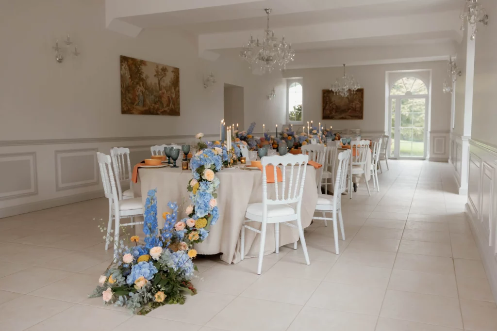 Tables rondes collées décorées de fleurs bleues et jaunes pour un dîner de mariage élégant.