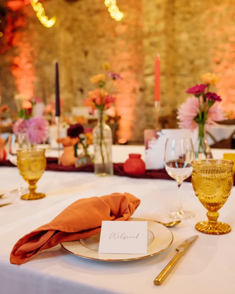 Détail d’une table de mariage au domaine de la Guérie (Normandie), associant serviette terracotta, verrerie ambrée et compositions florales Maison Magnolia pour illustrer la création d’une ambiance cohérente et élégante. Photo Audrey Guyon.