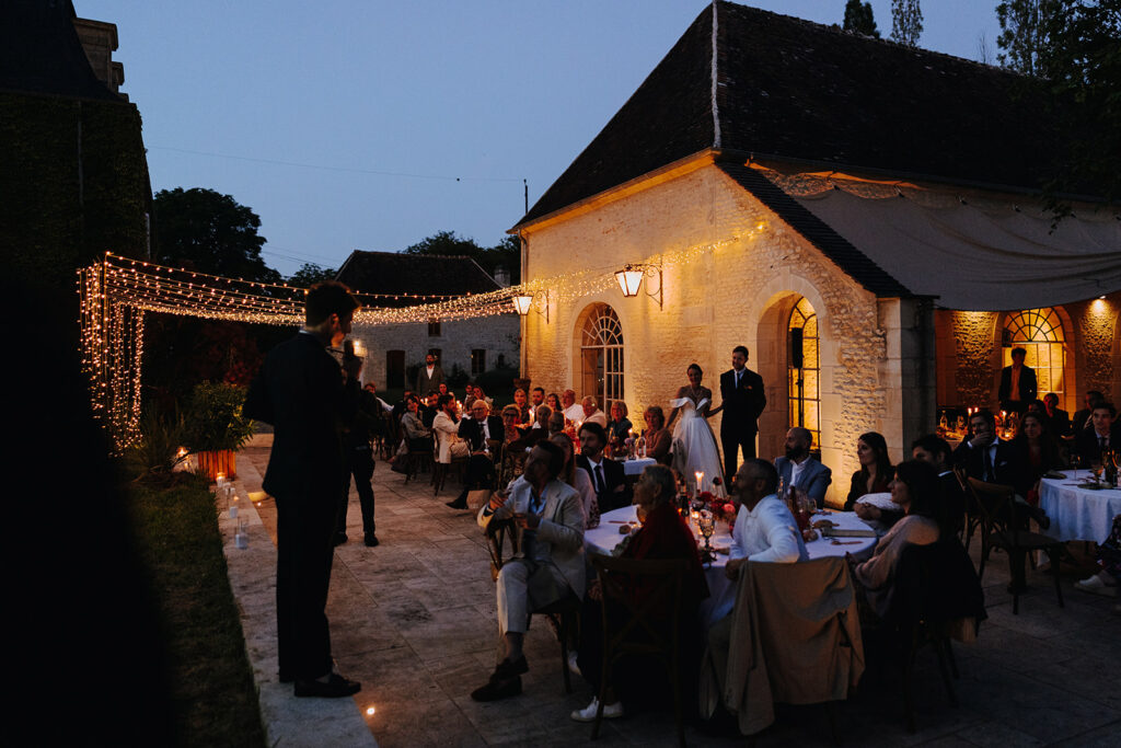 Dîner de mariage éclairé par des guirlandes lumineuses au Château de Tercey, montrant comment la lumière mariage transforme une soirée en extérieur. Photo Justine H Photography.