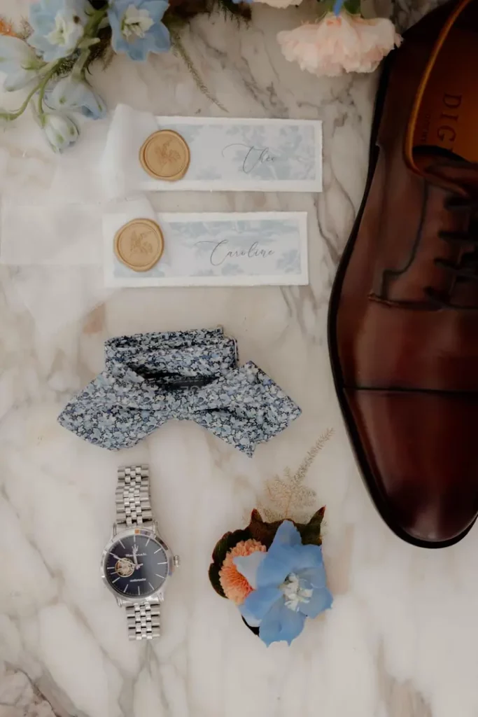 Accessoires des mariés, fleurs et papeterie réunis autour d'un même thème de mariage bleu et pêche.