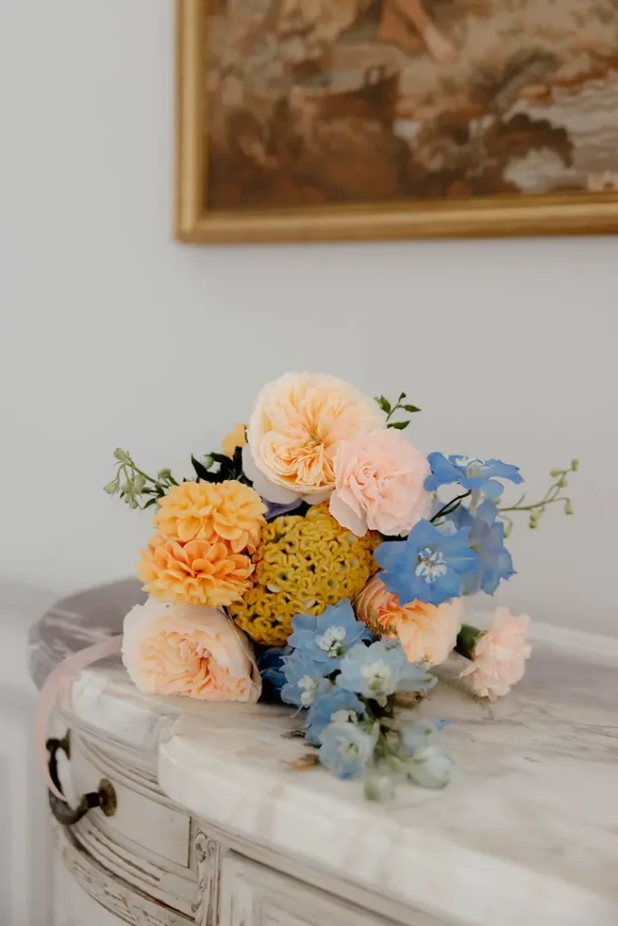 Composition florale bleu et pêche utilisée dans un thème de mariage élégant.