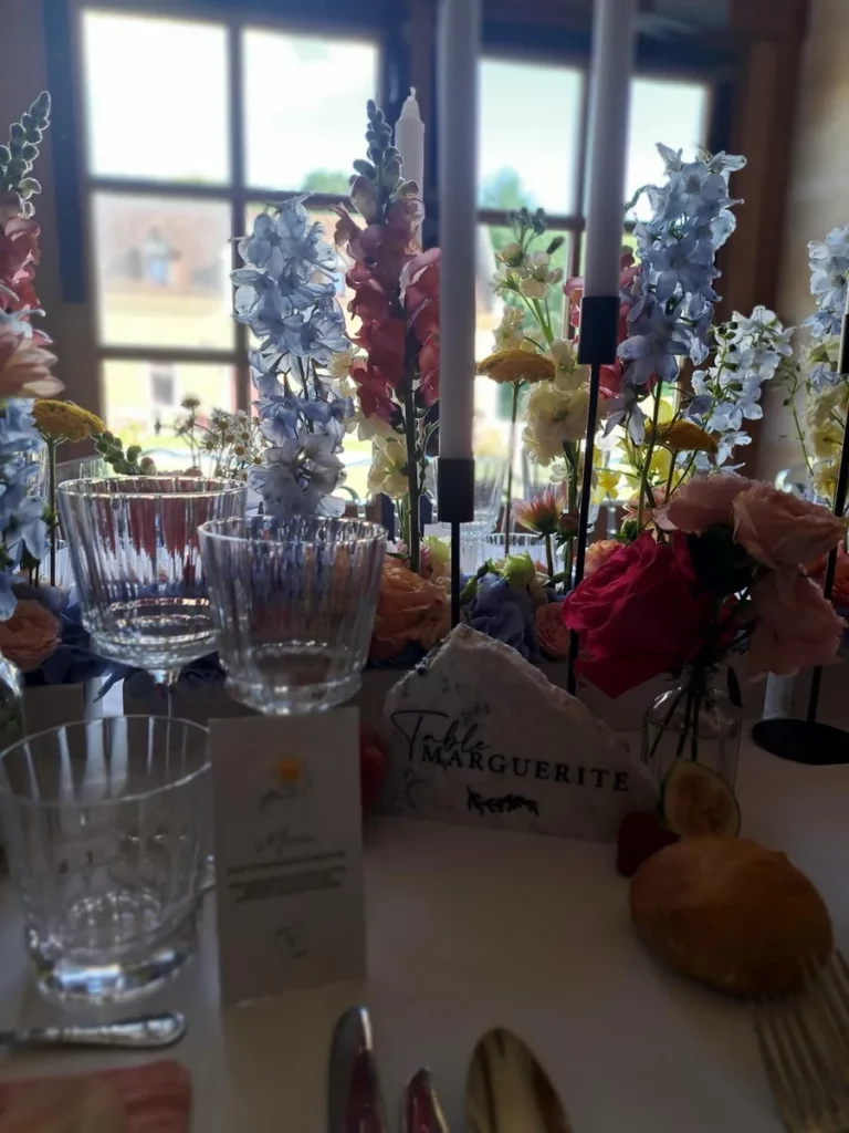 Table de mariage dressée où une carte de menu et un marque-table se fondent parmi les fleurs et les bougies. Faire participer ses proches à sa décoration de mariage