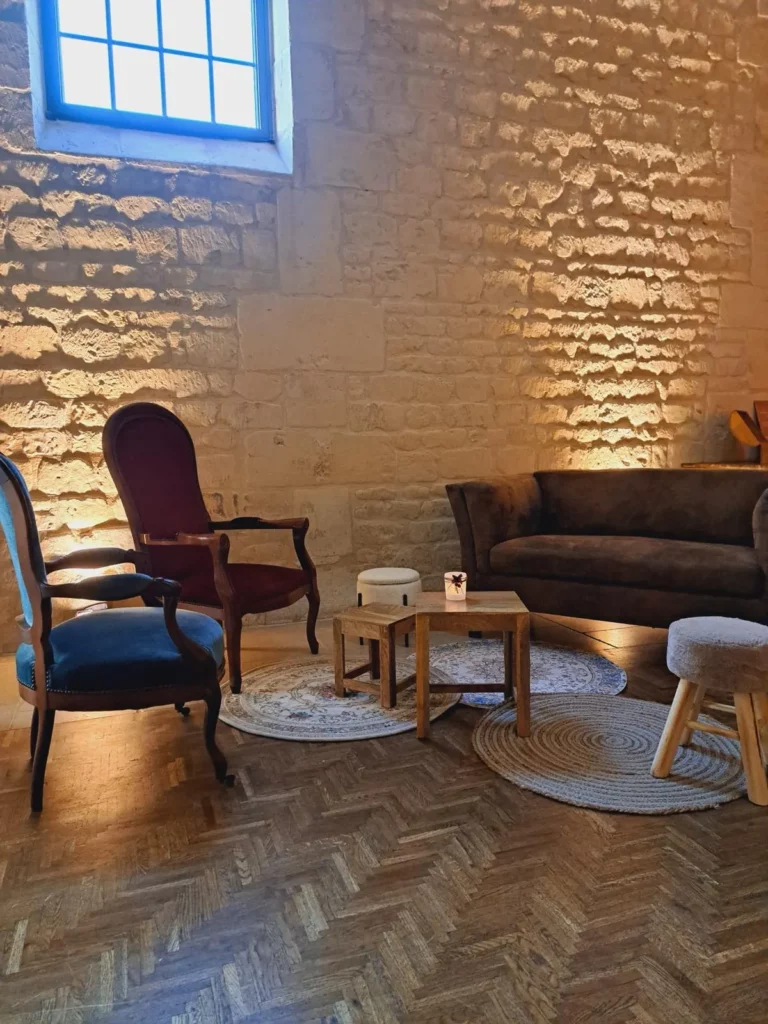 Espace lounge de mariage avec fauteuils anciens, canapé victorien et tapis superposés devant un mur de pierre Tout le budget est passé dans l'assise. Le mur reste brut, avec une seule source de lumière.