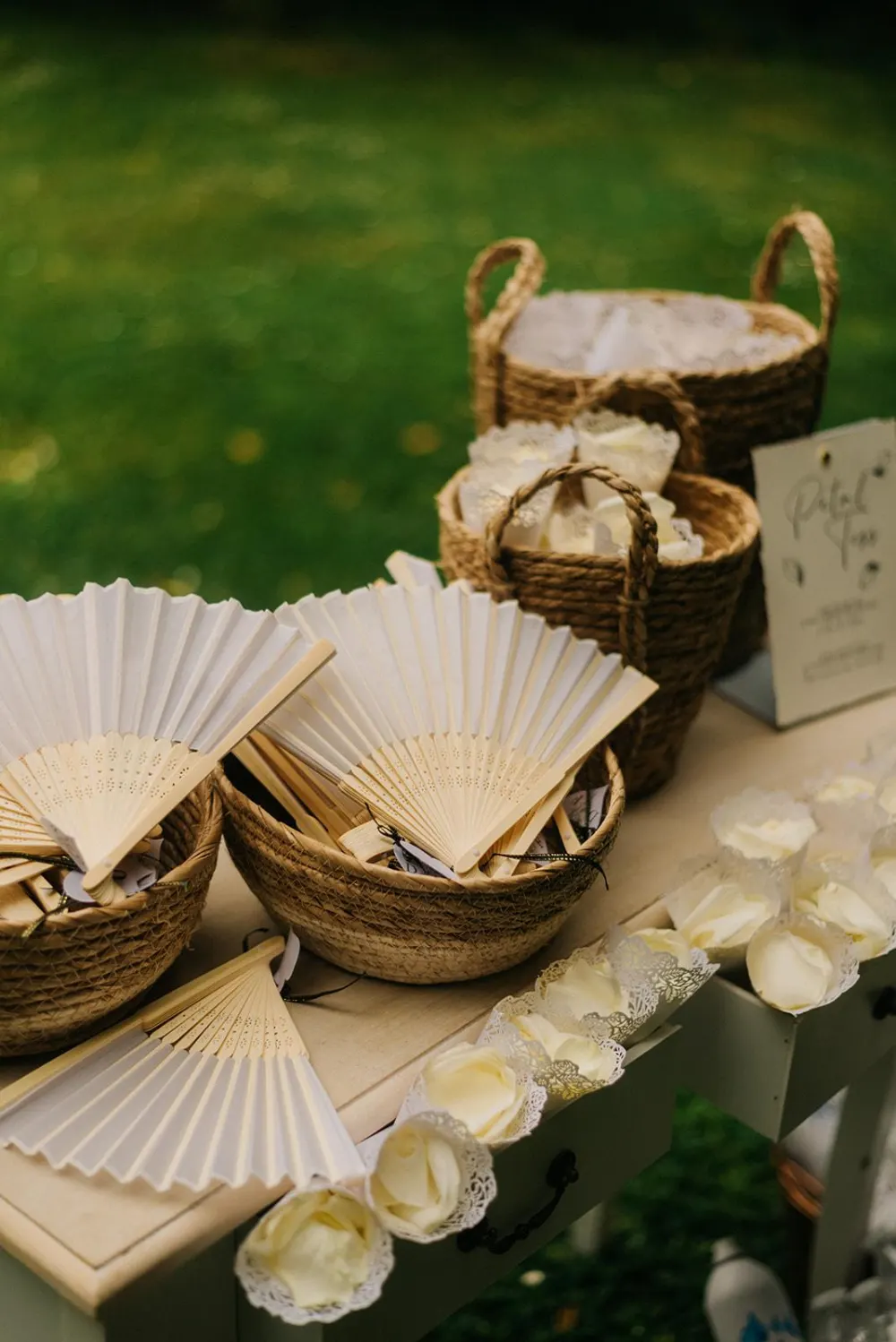 Éventails en bois et papier et cornets de pétales dans des paniers tressés, mariage au Manoir de Chivré