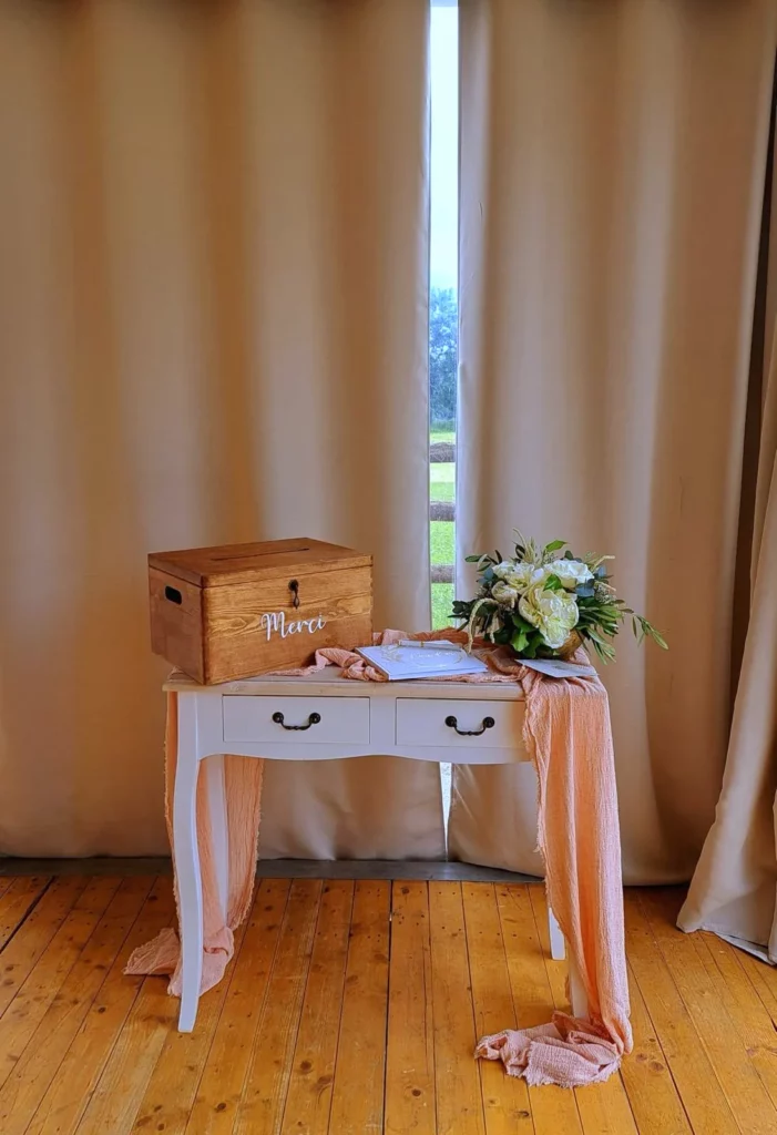 Console blanche accueillant un livre d'or de mariage, une urne en bois et un bouquet